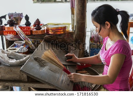 HUE, VIETNAM - CIRCA MARCH 2012: Young woman in pink shirt making manually incense sticks. She rolls the sticky stick on a heap of incense.