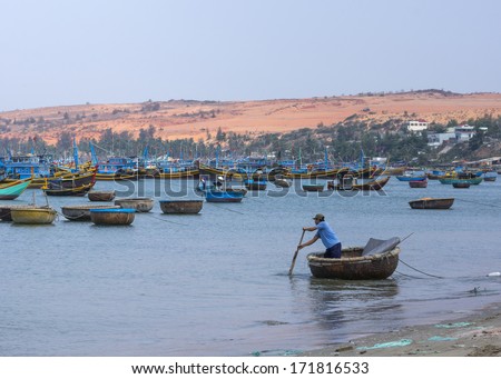 MUI NE, VIETNAM - CIRCA MARCH 2012: Man rows supplies to the fishing fleet anchored in front of the coast.