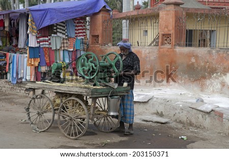 VARANASI, INDIA - CIRCA FEBRUARY 2011: Man with sugar cane pressing machine mounted on a cart. The mustached dark skinned man stands alone at his green machine.
