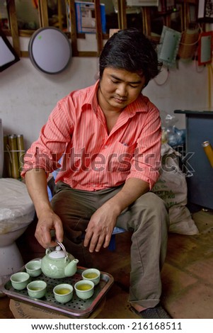 HANOI, VIETNAM - CIRCA MARCH 2012: Hardware store owner serving traditional tea to his customers as a welcome. Salmon colored shirt, green tea cups and a ceremonial gesture.