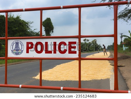 KUMBAKONAM, INDIA - OCTOBER 10, 2013: Tamil Nadu Police barrier protects drying corn on the public road, alerting traffic to drive around the patch of grain.