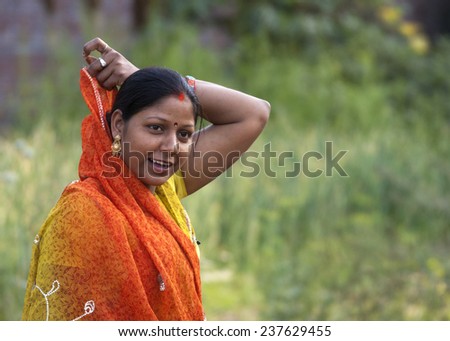 DANYALPUR, INDIA - FEBRUARY 27, 2011: Closeup of smiling young Hindu woman covering up her hair with an orange and yellow sari. The red stripe in her hair tells us she\'s married.