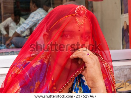 NAGAUR, INDIA - FEBRUARY 11, 2011: A young woman hides her face with a red, see-through veil and looks at the camera. She wears jewelry.