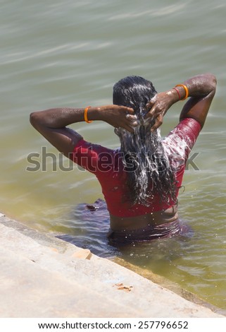 KUMBAKONAM, INDIA - OCTOBER 11, 2013: Young lady dressed in a red blouse washes her long, black hair in the sacred Maha Maham tank downtown.