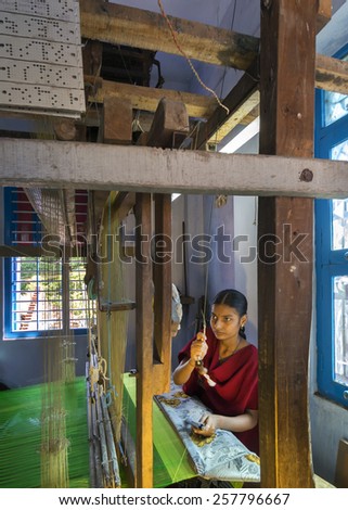 KUMBAKONAM, INDIA - OCTOBER 11, 2013: Home silk sari weaving on a hand loom set in a small room of the modest home. The young woman works on a green piece of textile.