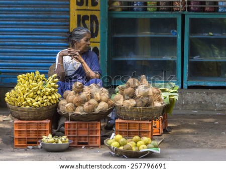 KUMBAKONAM, INDIA - OCTOBER 11, 2013: Graying female street vendor in blue sari sells coconuts, bananas and other fruits out of baskets in the street.