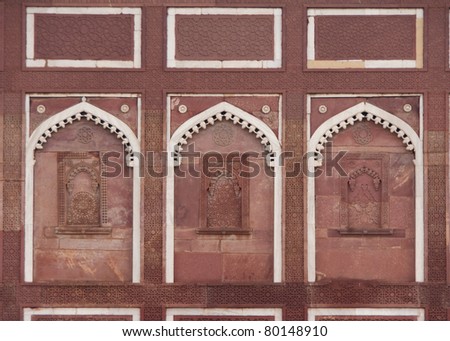Decorated wall with three false windows under white arch at Agra Fort Palace in India. Fine stone carvings in red sandstones trimmed by white lines.