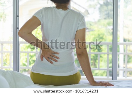 Closeup of young woman suffering from pain kidney disease while sitting on bed at home, Healthcare And Medicine concept