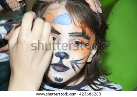 Little girl getting her face painted like a tiger by face painting artist