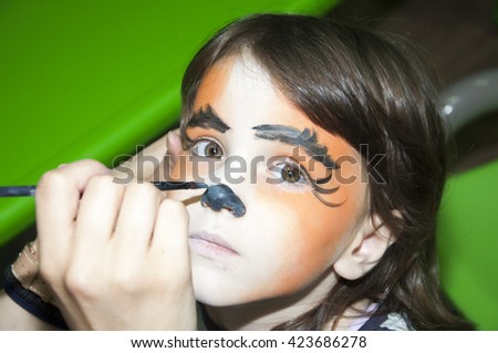 Little girl getting her face painted like a tiger by face painting artist