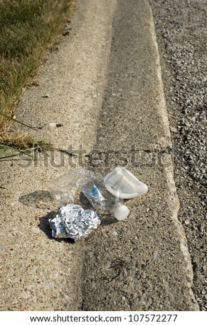 A crushed plastic bottle and aluminum foil create liter along a curb in the city.