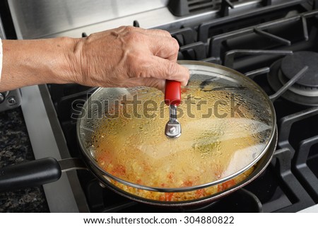 A woman pulls off the glass lid of a pan of fried Mexican rice.