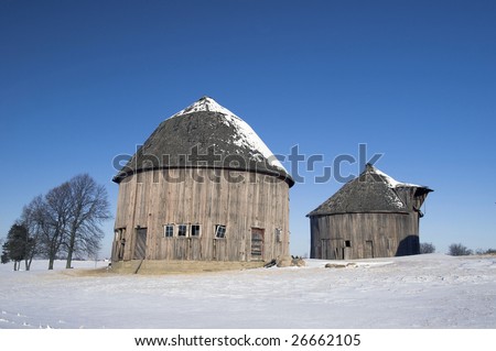 Two weathered round barns in a winter setting on a farm.