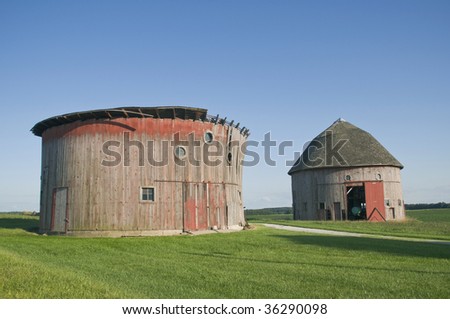 Two weathered round barns in a mowed farm field.