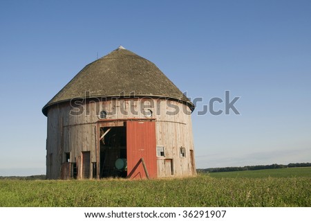 A weathered round barn sits in a mowed field.