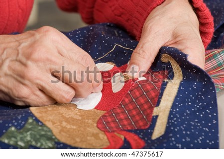 A quilter applies a blanket stitch with a needle and thread on a holiday quilt.