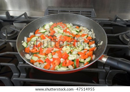A mixture of fresh veggies are sauteed in a pan to be used in a vegetarian pizza.