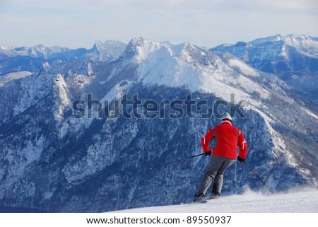 A skier in red jacket ski cross the slope with snowy mountains as background