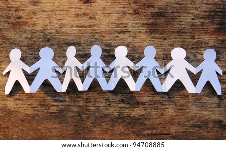 Group of paper chain people holding hands on the wood background