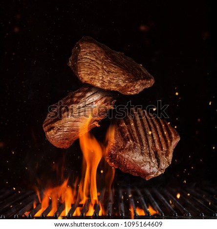 Flying pieces of beef rump steaks above grill flames, isolated on black background. Concept of flying food, very high resolution image