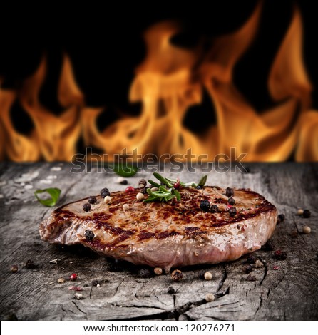 Delicious beef steak on wood with flames on background