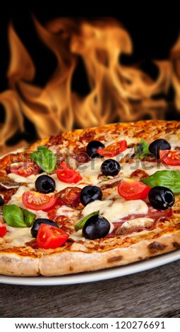 Delicious italian pizza served on wooden table with flames on background