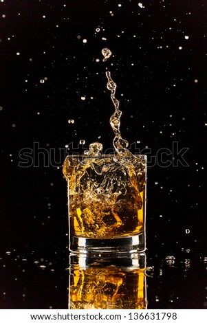 Isolated shot of whiskey splashing out of glass on black background