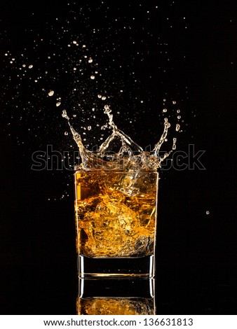 Isolated shot of whiskey splashing out of glass on black background