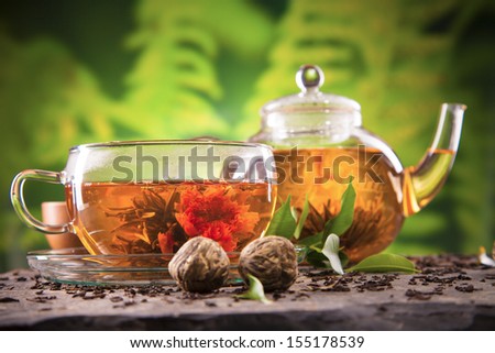 Cup of tea and teapot with blooming tea on blur green background