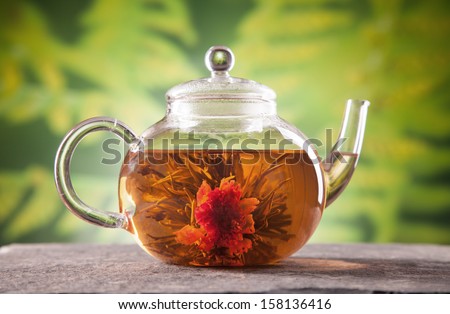 Teapot with blooming tea on blur green background