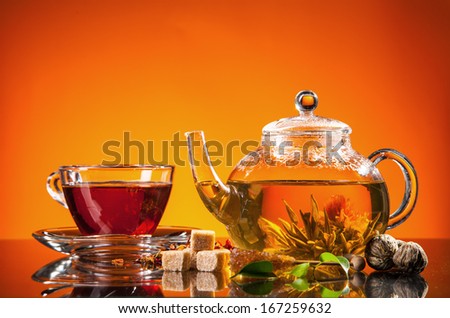 Teapot and cup with blooming tea on glass