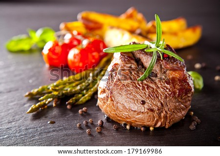 Piece of red meat steak with vegetable and herbs, served on black stone surface.