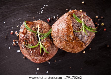 Pieces of red meat steaks with rosemary served on black stone surface. Shot from upper view