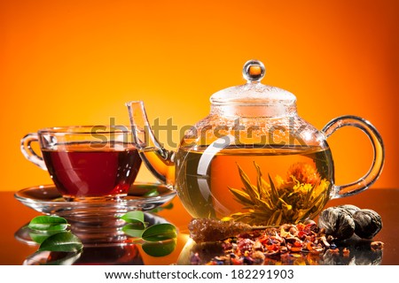 Teapot and cup with blooming tea on glass