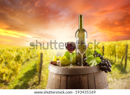 Old wooden keg with bottle and glass of red, white wine. Rural vineyard on background