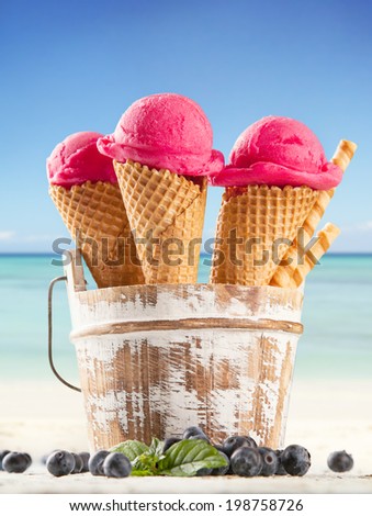 Fresh fruit ice cream scoops in cones, blur beach on background
