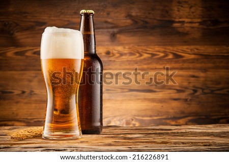 Glass and bottle of beer with wheat ears on wooden planks