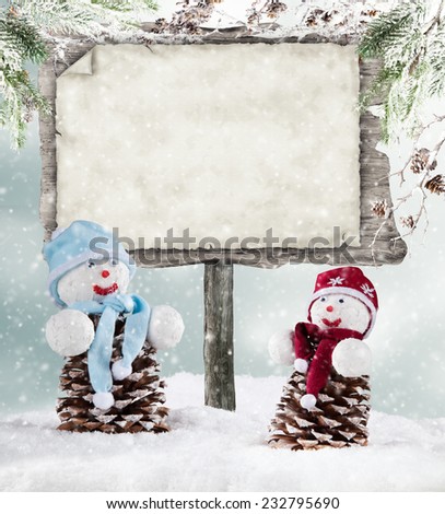 Winter holiday happy snow men with blur landscape on background. Empty wooden board for copyspace