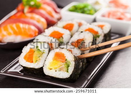 Delicious sushi rolls served on black plate and stone