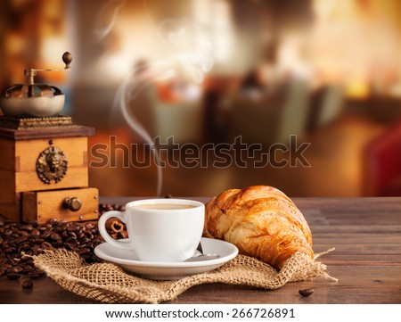 Coffee drink served with croissant on wooden table with blur cafeteria as background