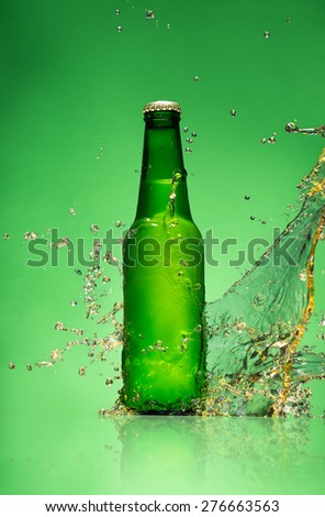 Bottle of beer with splash around on green background.