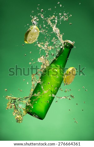 Bottle of fruit beer with splash around on green background.