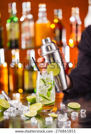 Mojito cocktail drink on bar counter with barman holding shaker on background