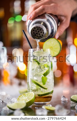 Mojito cocktail drink on bar counter with barman holding shaker on background