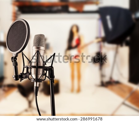 Detail of singing microphone in studio with blur guitar player on background