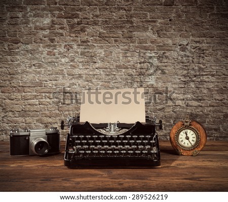 Retro typewriter, alarm-clock and camera placed on wooden planks. Old brick wall as background with copyspace.