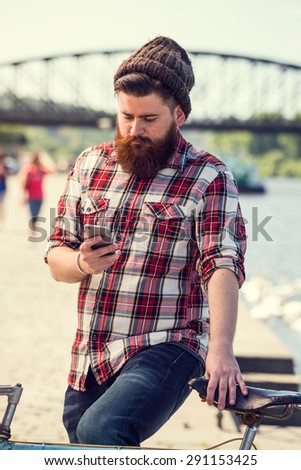 Trendy hipster young man with bicycle using smart phone. Posing next to river