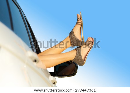 Summer road trip car vacation concept. Woman legs out the windows in car. Conceptual freedom, travel and holidays image with copy space.