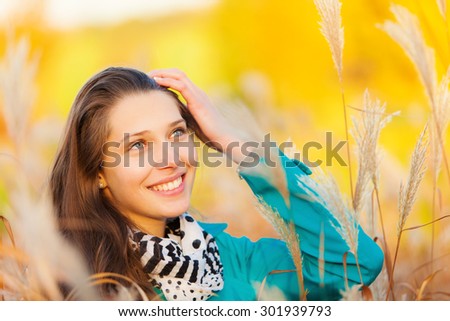 Beautiful brunette girl sitting in autumn grass with smilling face. Concept of happiness and joy