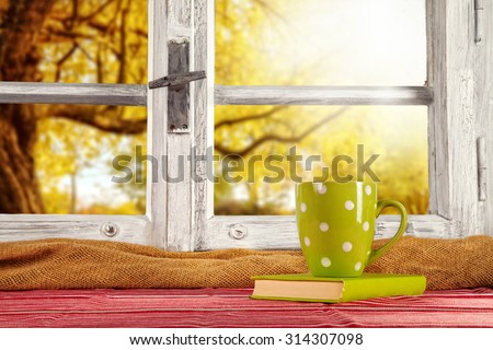 Vintage wooden window overlook autumn trees, shot from cottage interior with cup of tea and book